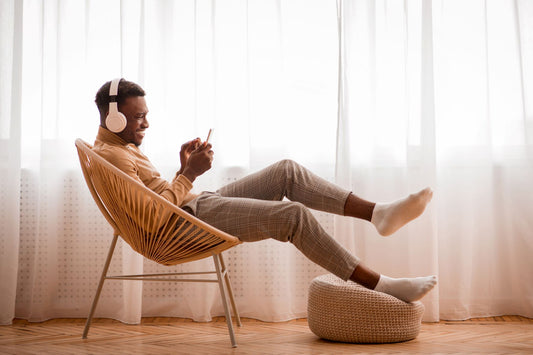 A young african american man leans back in a chair. He's listening to music and looking at his phone