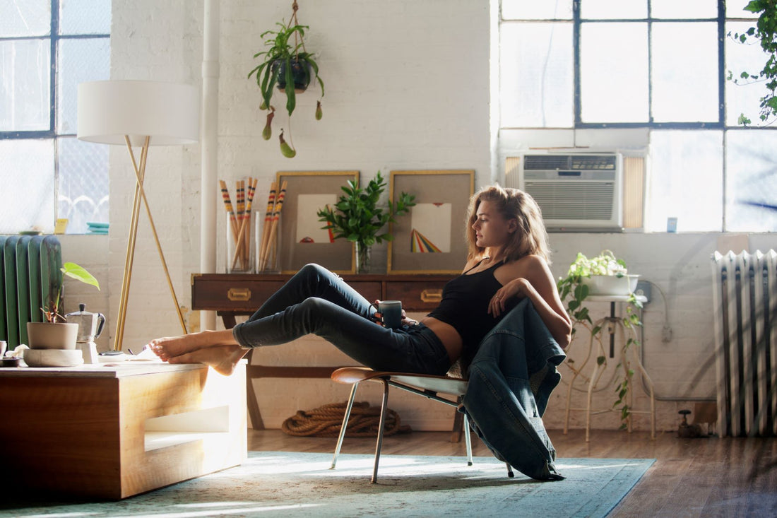 A young woman in jeans and a crop top is in an art studio is leaning back in a chair. 